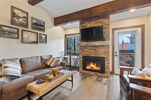 Ein gemütliches Wohnzimmer mit Kamin, einer Couch, einem Couchtisch und einem an der Wand befestigten Fernseher.