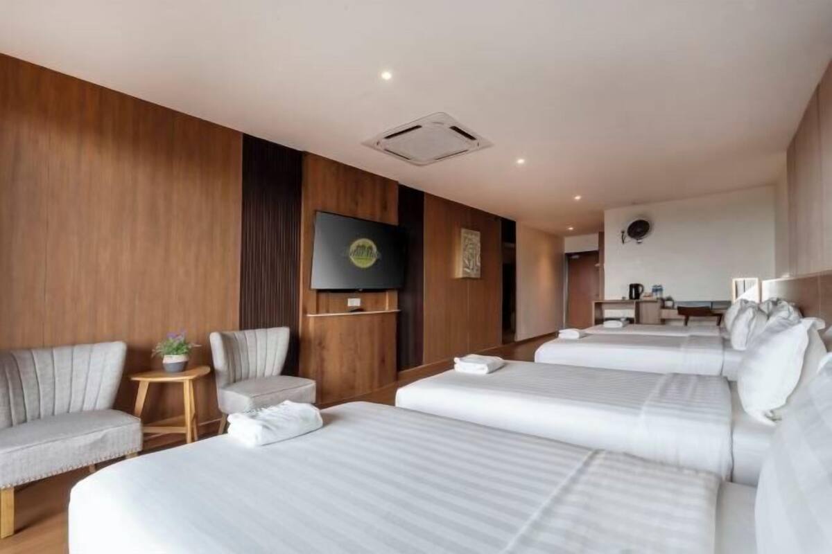 A hotel room with three beds, a TV, a desk, and a small table with a plant.