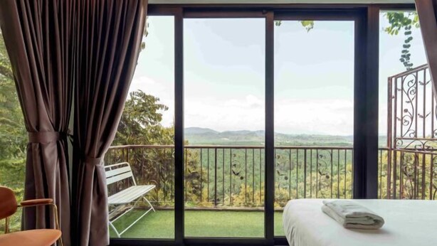 Ein Schlafzimmer mit einer großen Schiebeglastür, die auf einen Balkon mit Blick auf Grünflächen und Hügel führt.