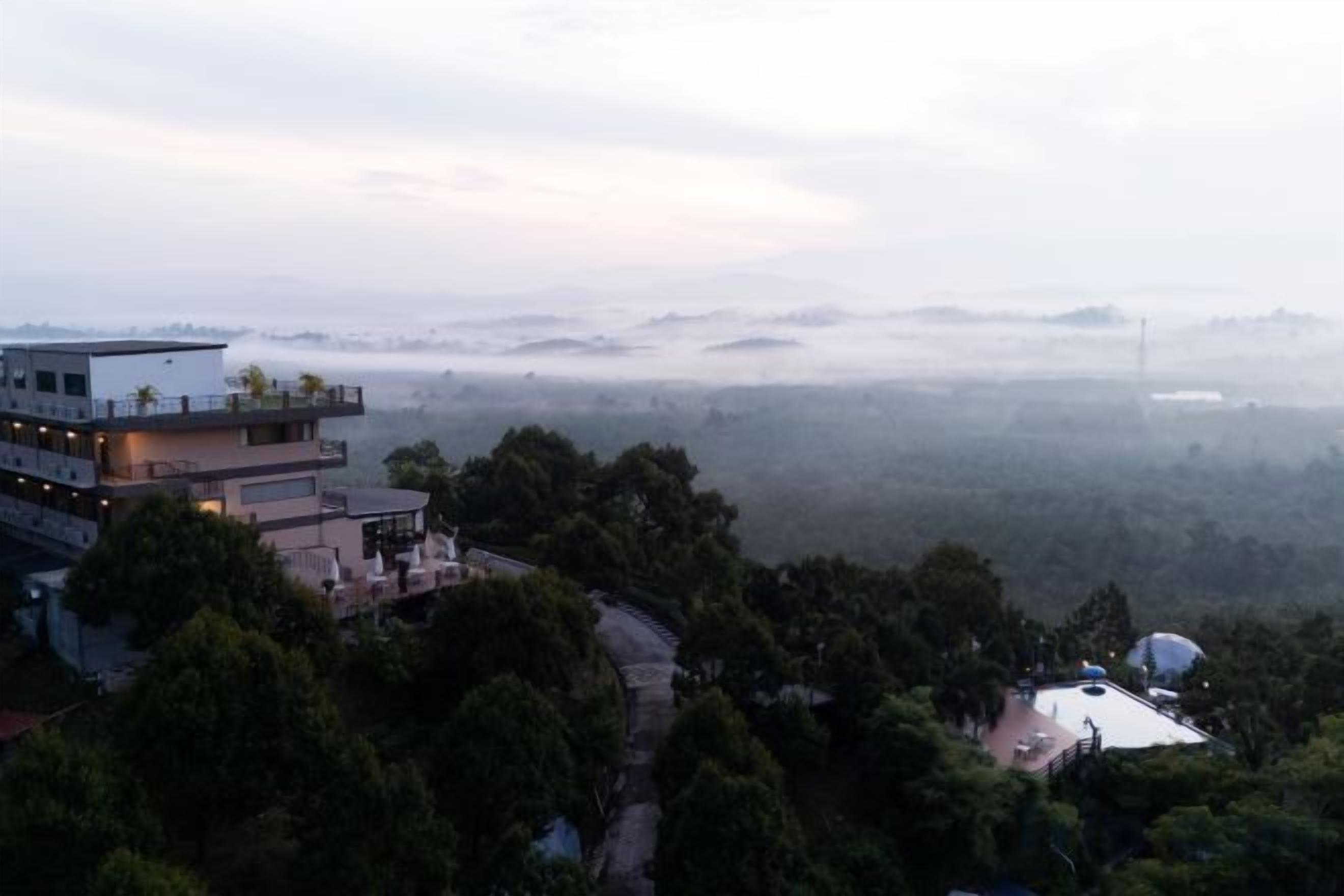 A multi-story building with a rooftop terrace, surrounded by dense forest and misty hills.