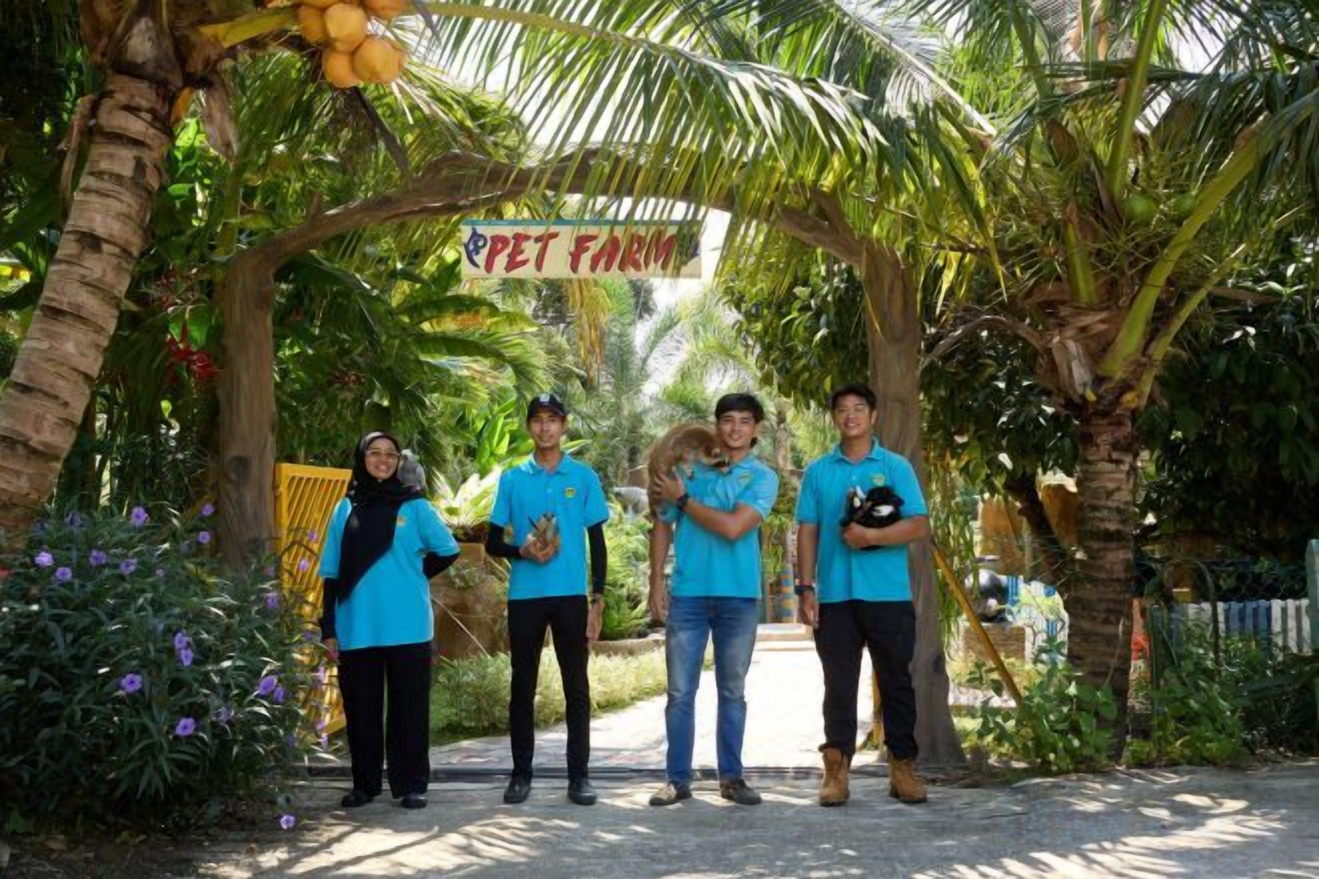 A group of people standing under a sign that reads 'PET FARM' in a garden setting with palm trees and plants.