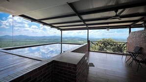 Eine Dachterrasse mit einem Endlos-Glaspool, einem Ziegelkamin und Blick auf ferne Berge.