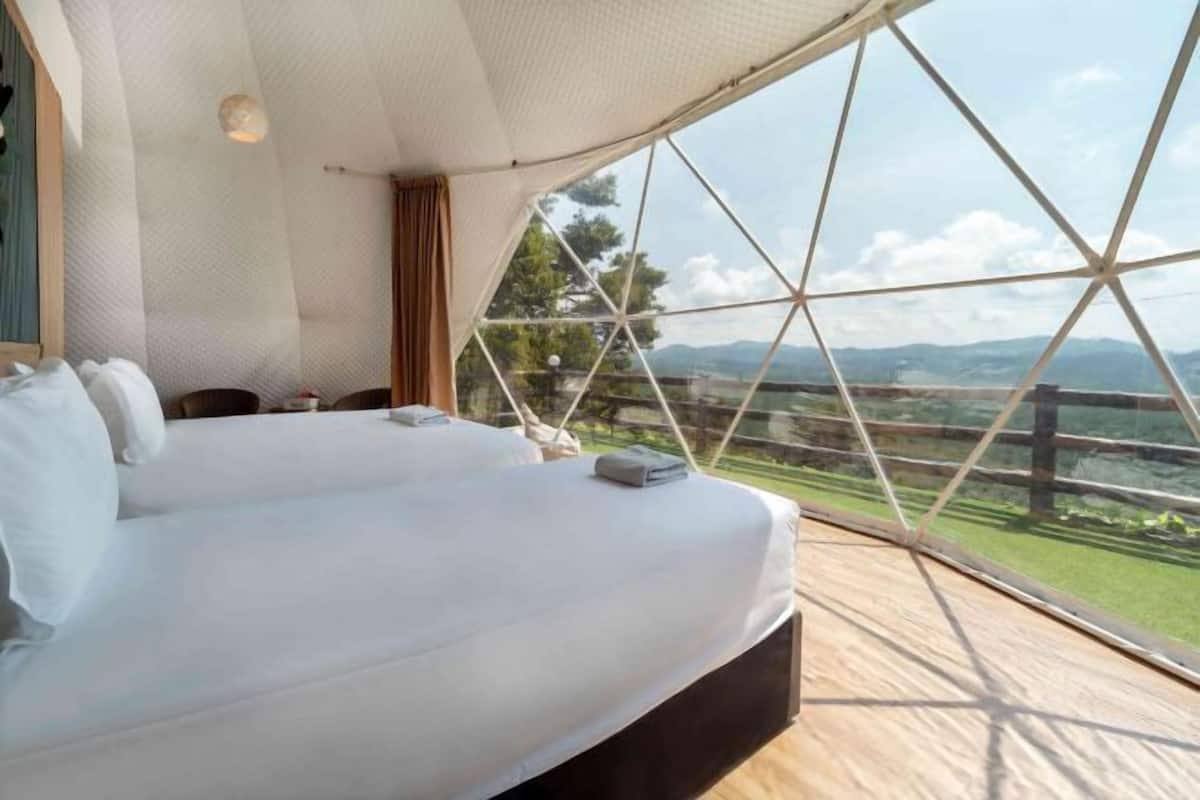 A bedroom with a large bed, a view of the outdoors through a geometric window, and a wooden floor.
