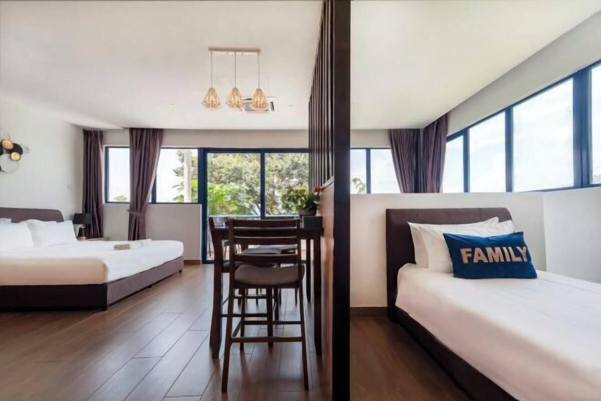 A hotel room with two beds, a dining table with chairs, and large windows.