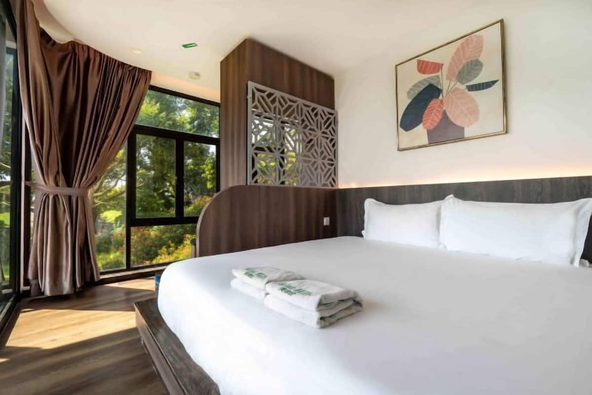 A hotel room with a large bed, a window with curtains, a decorative wall panel, and a framed artwork.