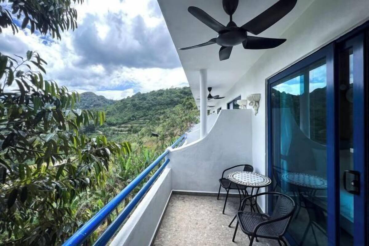 A balcony with a ceiling fan, a table with chairs, and a view of a lush landscape.