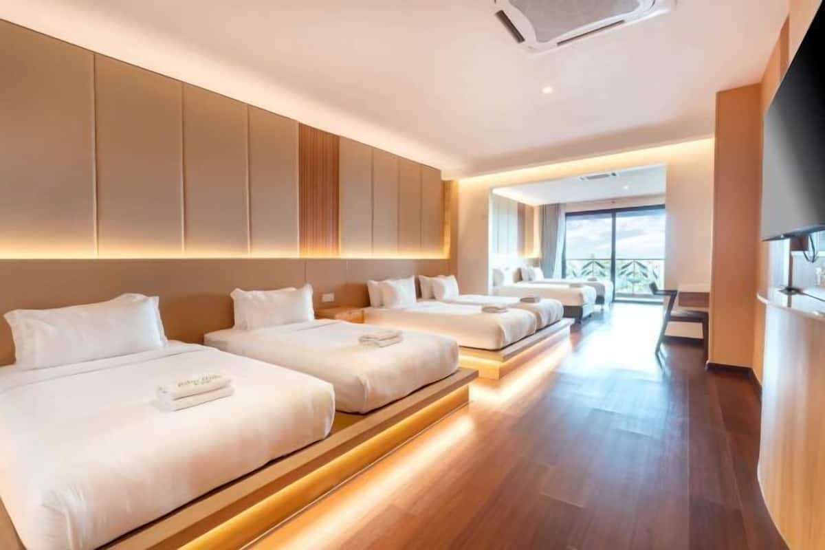 A hotel room with three beds arranged in a row, a TV on the right, and a balcony with a view.