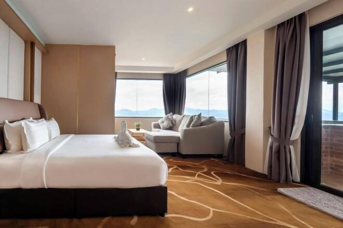 A hotel room with a large bed, a sofa, a view of the mountains, and a large window with curtains.