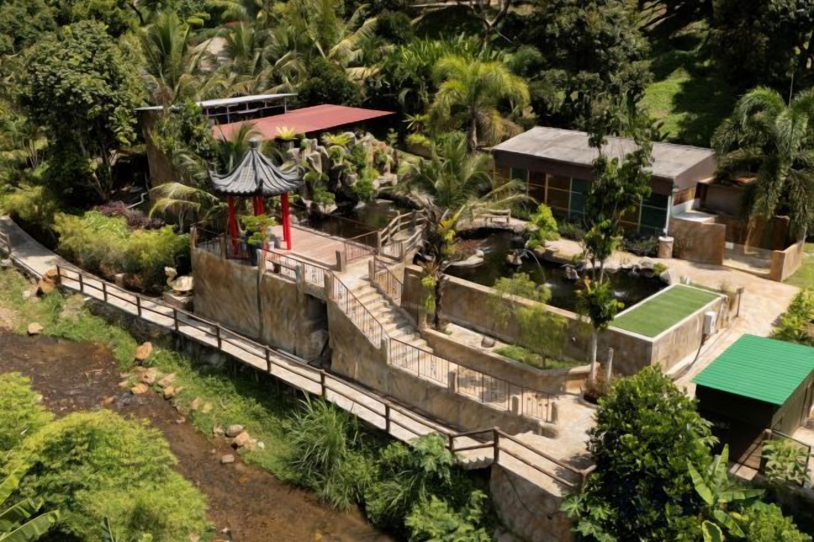 A garden with a gazebo, a bridge, and a building with a red roof.