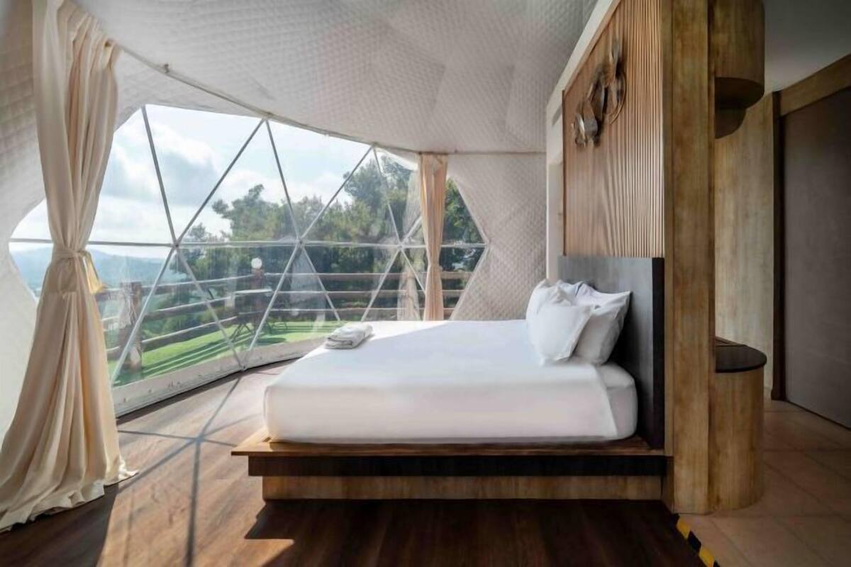 A bedroom with a large window, a bed, and wooden flooring.