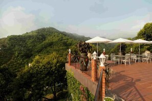 An outdoor terrace with tables and umbrellas, overlooking a hilly landscape. - Bilut Hills - Eco Resort (Teras)
