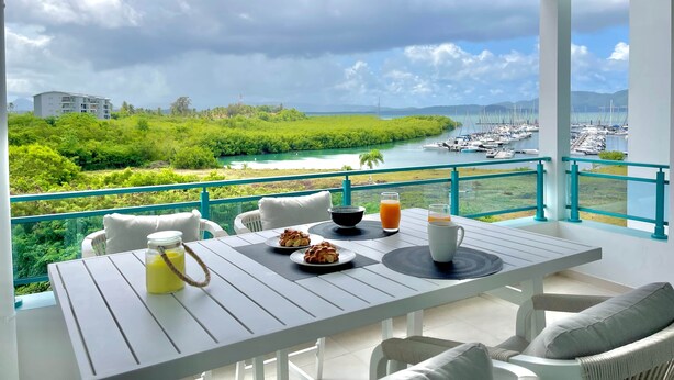 A balcony with a table set for breakfast, overlooking a marina and greenery.
