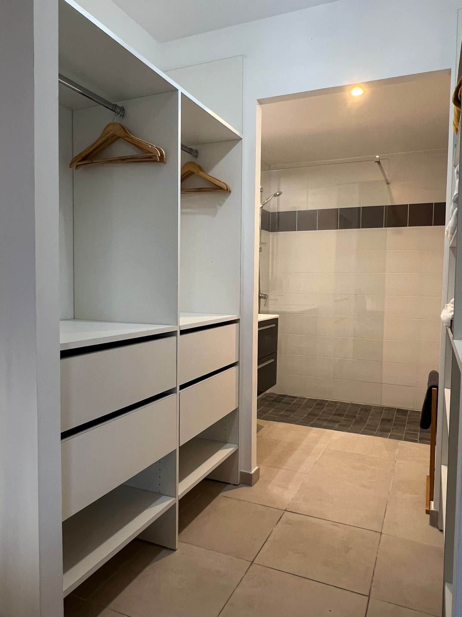Un dressing accessible sans porte, doté d’étagères ouvertes, d’une tringle à vêtements et d’un espace douche aux murs carrelés.