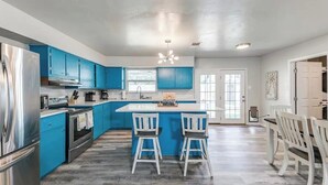 A modern kitchen with blue cabinets, a stainless steel refrigerator, and a central island with bar stools. - Cozy 6 bed - 3 bath home close to Main Street (Fredericksburg)