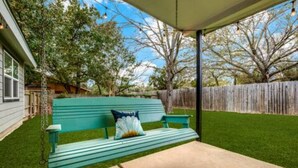 A green outdoor seating area with a swing, a wooden fence, and a house in the background. - Cozy 6 bed - 3 bath home close to Main Street (Fredericksburg)
