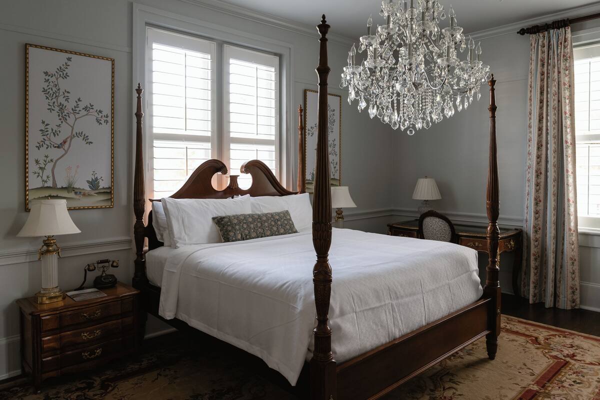 Una cama con dosel, una lámpara de noche con una lámpara y un cuadro floral en la pared.