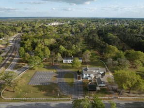 An aerial view of a residential area with a large house, a parking lot, and surrounding greenery.
