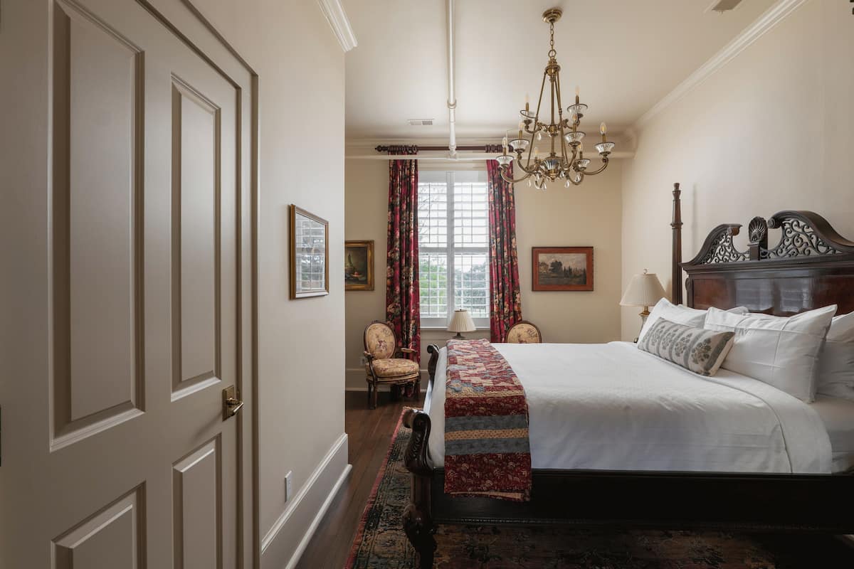 Un dormitorio con una cama grande, una araña, una silla y una ventana con cortinas.