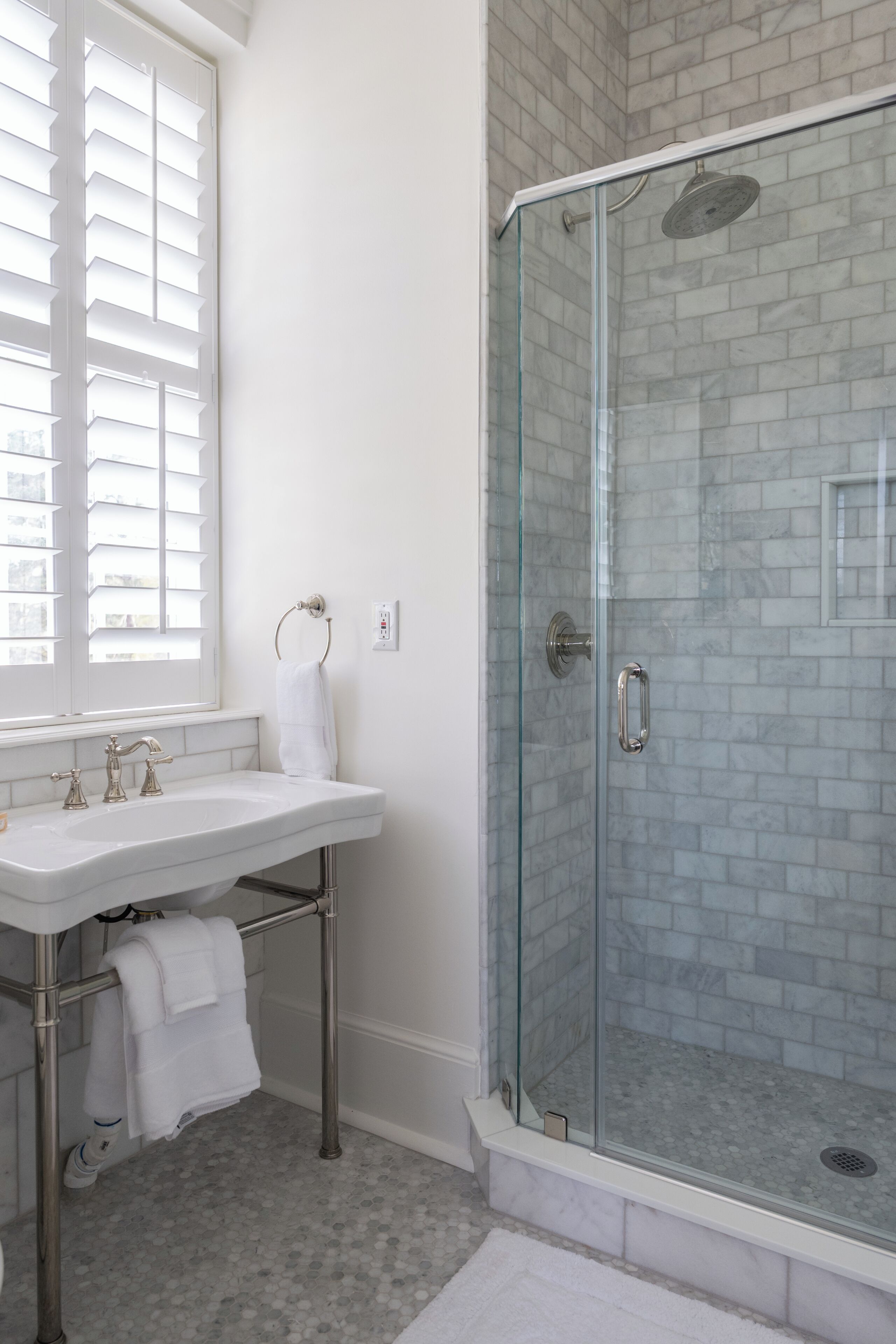 A bathroom with a glass-enclosed shower, a sink with a towel rack, and a window with blinds.