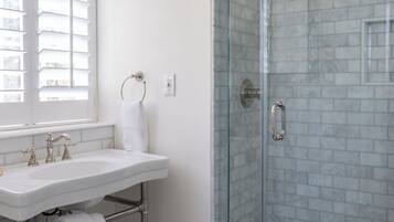 A bathroom with a glass-enclosed shower, a sink with a towel rack, and a window with blinds.