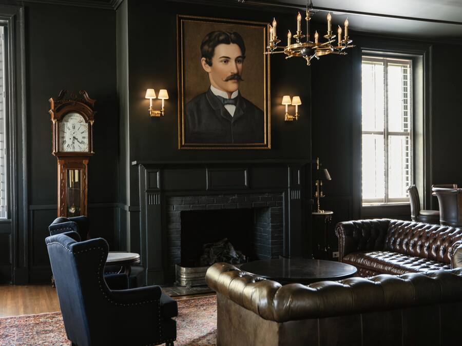 Una habitación con chimenea, un retrato grande, un reloj y un sofá de cuero.
