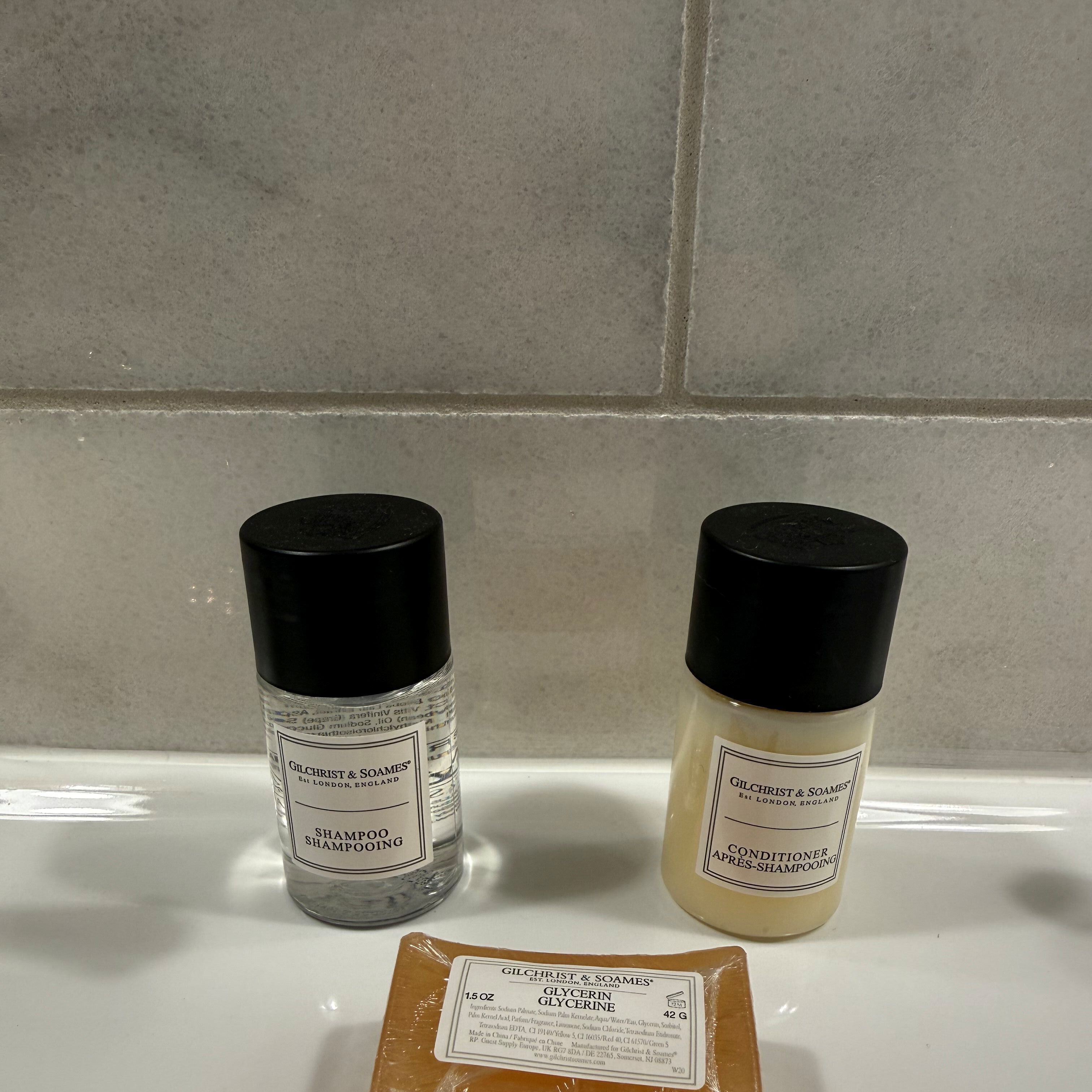 Two bottles of Gilchrist & Soames shampoo and a bar of glycerin soap on a bathroom counter.
