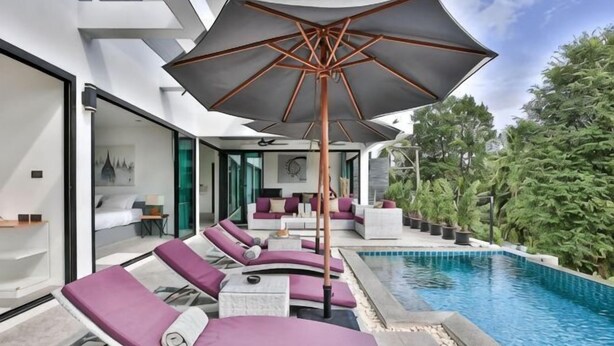 Zona de piscina exterior moderna amb gandules, un parasol gran i vistes a la vegetació circumdant.