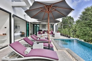 A modern outdoor pool area with lounge chairs, a large umbrella, and a view of the surrounding greenery. - Villa Hayou, Lamai Koh Samui (Koh Samui)