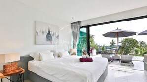 Habitació d'hotel moderna amb un llit gran, una taula auxiliar, una làmpada, un coixí decoratiu i vista a l'exterior amb ombrel·les i cadires.