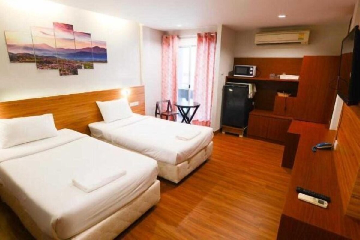 A hotel room with two beds, a kitchenette, a TV, and a painting on the wall.
