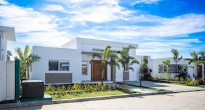 A modern residential building with a clean, white exterior, a well-maintained lawn, and a clear blue sky.
