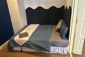 Una cama bien hecha con una colcha azul y gris, una almohada blanca y una manta doblada a un lado.
