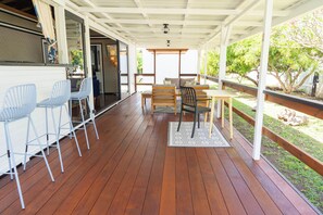 A covered outdoor patio with wooden flooring, a table with chairs, and a seating area. - Fare Manea - Authentic Polynesian Bungalow in Paea (Pā'ea)