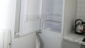 Una cocina compacta con refrigerador integrado, hervidor y encimera de mármol.