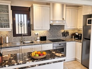 A modern kitchen with white cabinetry, a granite countertop, a built-in oven, and a stainless steel refrigerator.