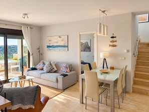 Una sala de estar moderna con sofá, mesa de comedor y sillas, una escalera y un balcón con vistas.