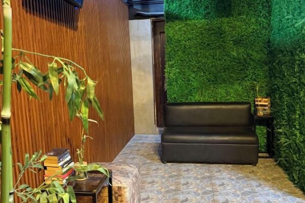 Una habitación con pared de madera, pared verde, sofá negro y una pequeña mesa con libros y una planta.