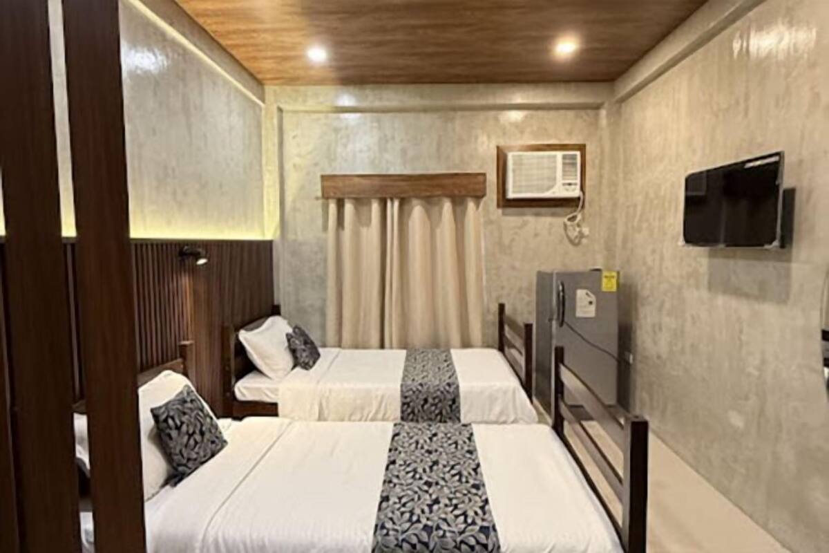 Een hotelkamer met twee bedden, een houten hoofdbord, een aan de muur bevestigde televisie en een raam met gordijnen.