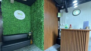 A reception area with a green wall, a wooden reception desk, a black sofa, and a guitar. - HM Eco Hotel Naia (Pasay)