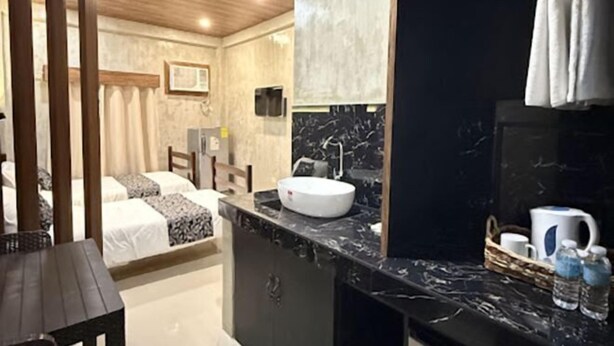 A bedroom with a bed, a bedside table, a nightstand, a mirror, and a bathroom with a sink and a towel rack. - HM Eco Hotel Naia (Pasay)