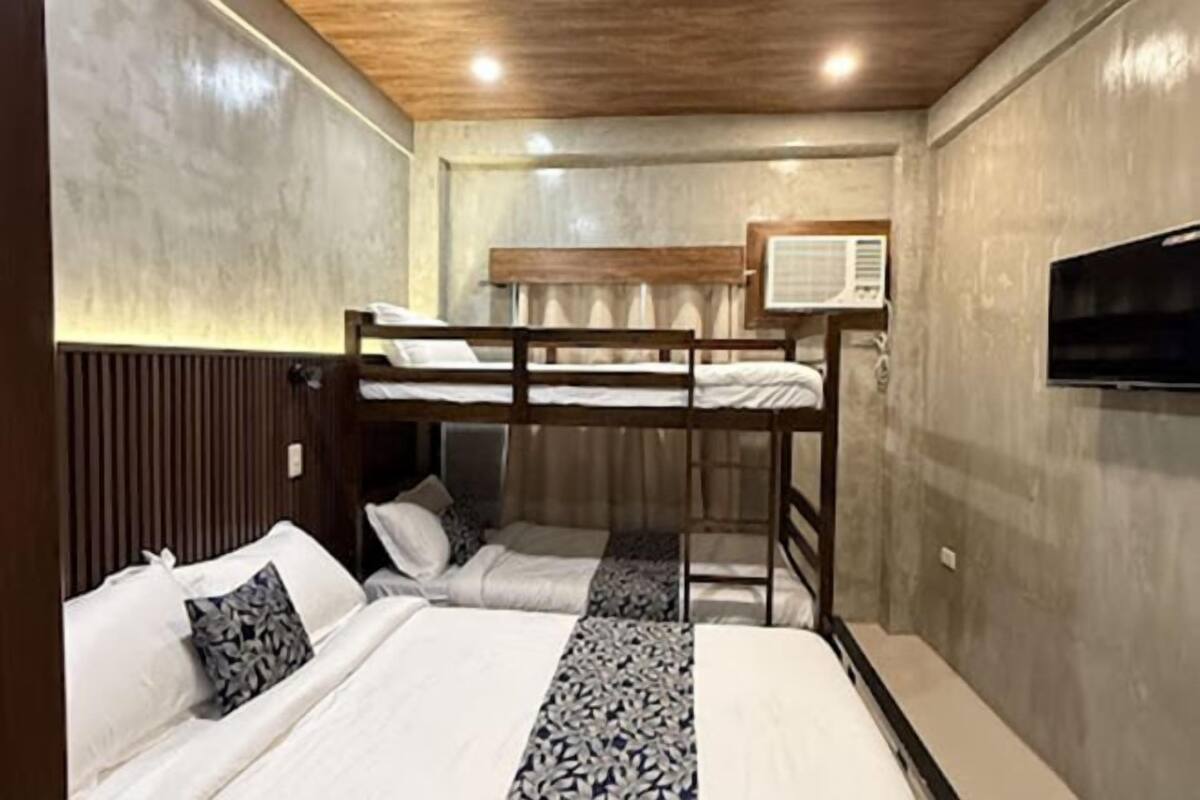 Een slaapkamer met stapelbed, houten hoofdeinde, een wandtelevisie en een raam met gordijnen.
