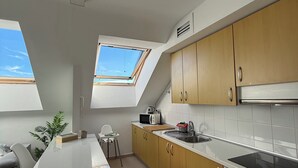 A modern kitchen with a skylight, wooden cabinets, a white countertop, and a built-in oven. - The Attic (Moya)