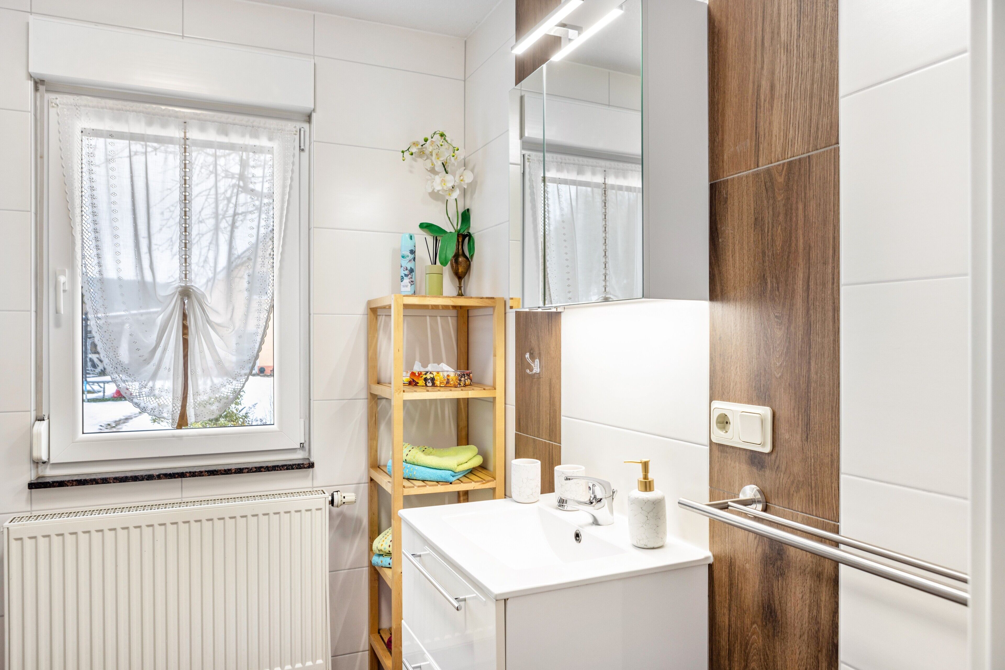 Un baño con ventana, espejo, repisa con artículos de aseo y toallero.