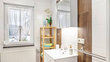 Un baño con ventana, espejo, repisa con artículos de aseo y toallero.