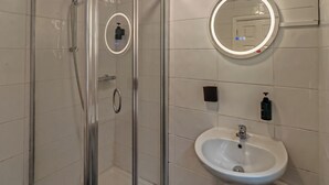 Une salle de bain moderne avec une douche à parois de verre, un lavabo blanc et un miroir rond avec éclairage intégré.