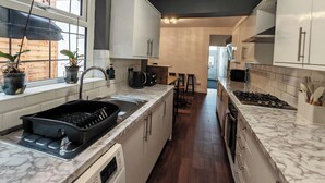 Une cuisine moderne avec des meubles blancs, un plan de travail en marbre, un four encastré et une fenêtre agrémentée de plantes en pot.