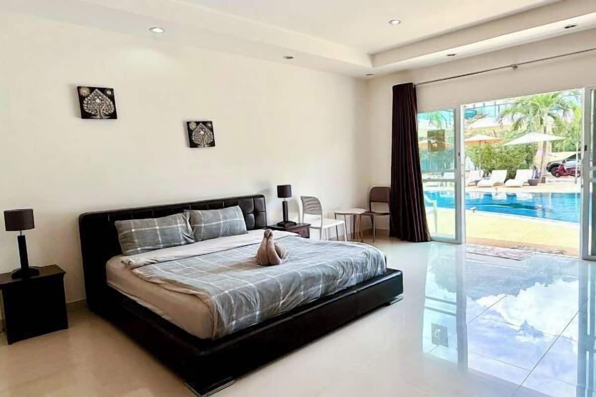 Une chambre moderne avec un grand lit, une table de chevet, un bureau et une vue sur une piscine, visible à travers de grandes portes coulissantes.