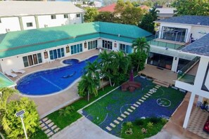 Une piscine entourée d’une cour plantée de palmiers, un court de tennis et un bâtiment doté d’un toit végétalisé.