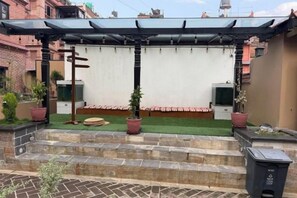 Un patio techado con techo plano, escalones de piedra que conducen a una pared blanca y plantas en macetas.