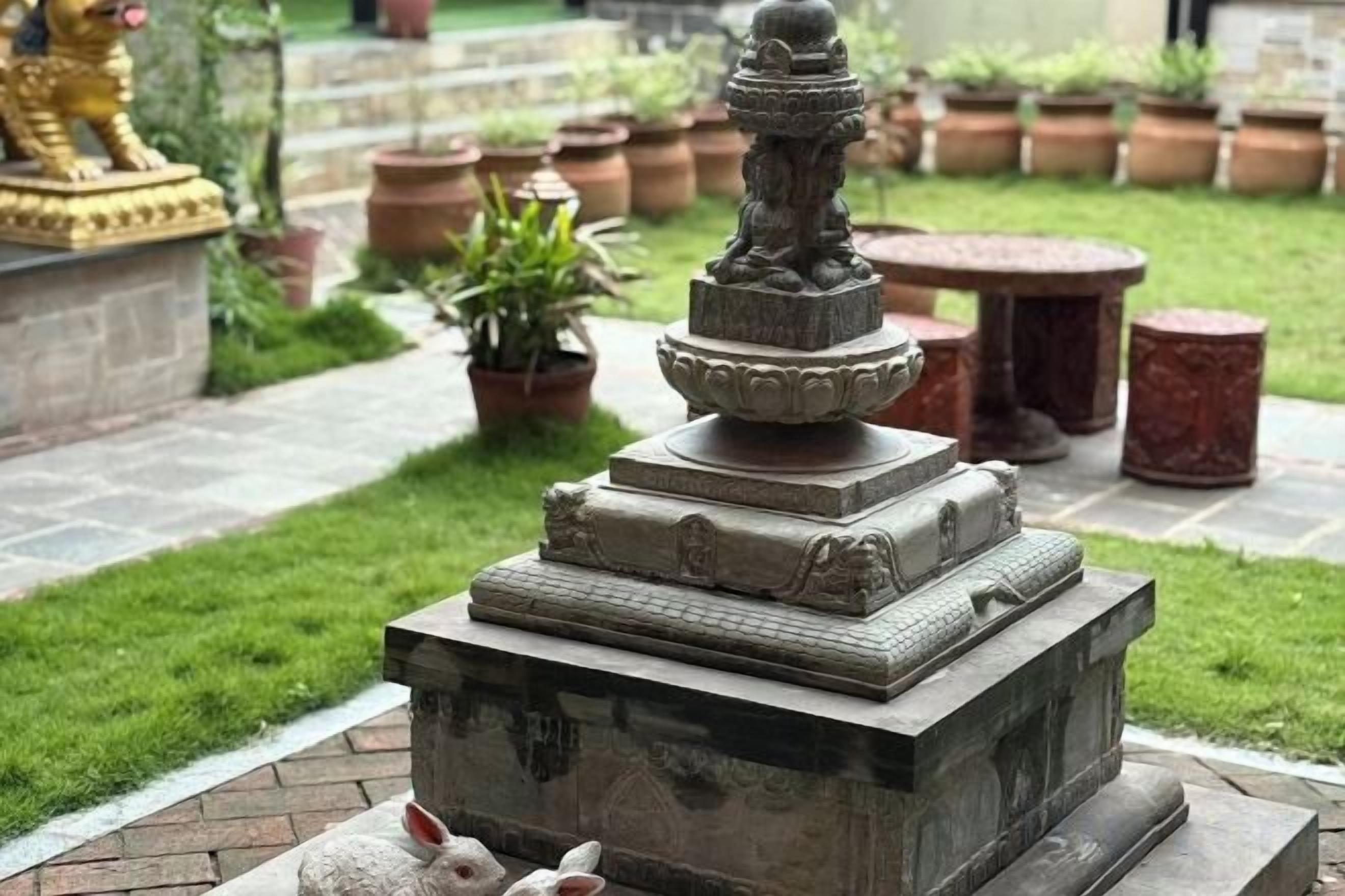 Un jardín con una fuente de piedra, plantas en macetas y una estatua.